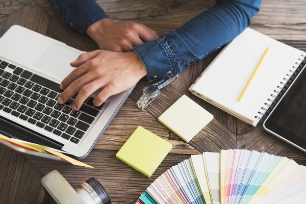 Man working on the laptop and open diary, colors templates and sticky notes on the table